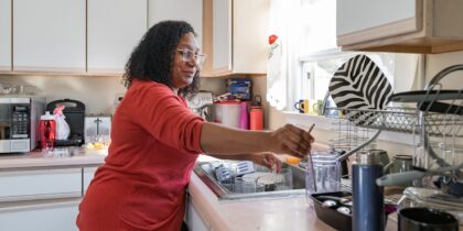 Black woman wearing red jumper doing the washing up at home.