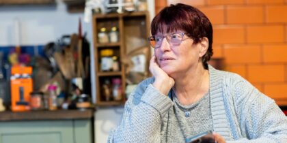 Older woman with dyed red hair and grey top sits in kitchen