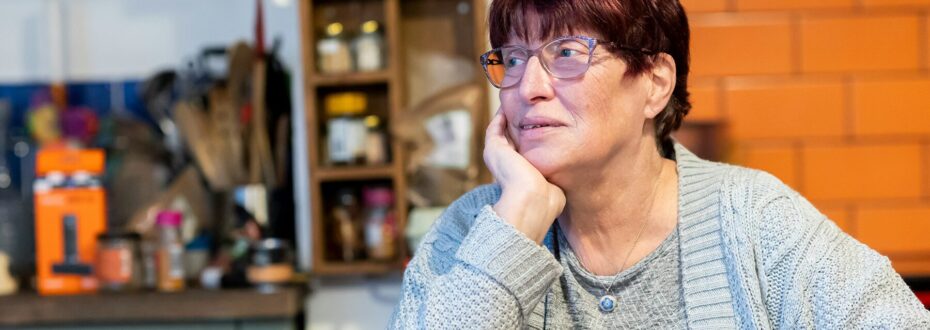 Older woman with dyed red hair and grey top sits in kitchen