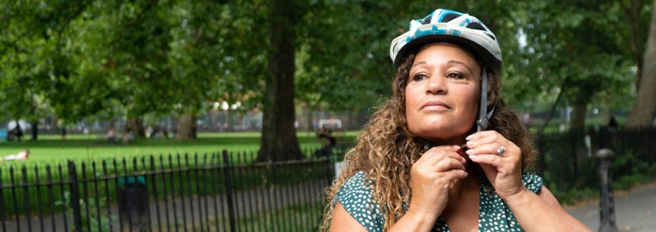 Black woman in green top looks away as she fastens her bike helmet