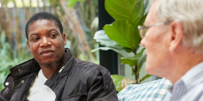 A Black man wearing a black jacket is sitting facing an older white man