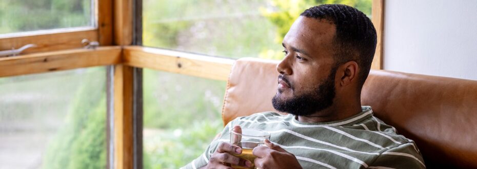 Young man sits in leather arm chair, holding a cup of tea and looking out a window
